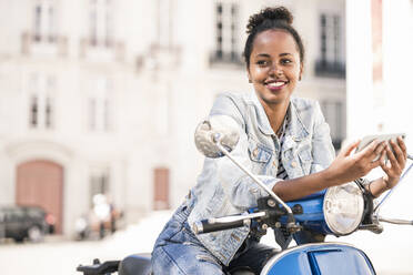 Lächelnde junge Frau mit Motorroller und Mobiltelefon in der Stadt, Lissabon, Portugal - UUF19204