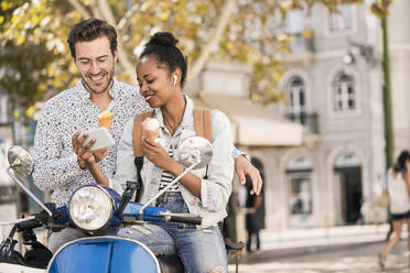 Lächelndes junges Paar mit Motorroller und Eiscreme beim Telefonieren in der Stadt, Lissabon, Portugal - UUF19209