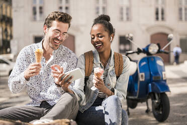 Happy young couple with ice cream using mobile phone in the city, Lisbon, Portugal - UUF19211
