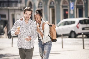 Glückliches junges Paar mit Eis und Mobiltelefon in der Stadt unterwegs, Lissabon, Portugal - UUF19216