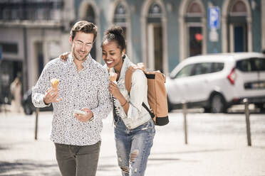 Happy young couple with ice cream and mobile phone in the city on the go, Lisbon, Portugal - UUF19216