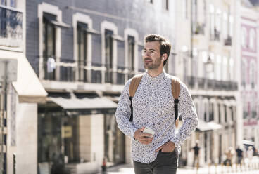 Smiling young man with wireless earphones in the city on the go, Lisbon, Portugal - UUF19218