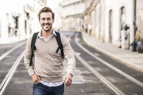 Portrait of smiling young man with backpack in the city on the go, Lisbon, Portugal stock photo