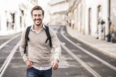 Portrait of smiling young man with backpack in the city on the go, Lisbon, Portugal - UUF19241