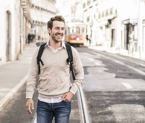 Glücklicher junger Mann mit Rucksack in der Stadt unterwegs, Lissabon, Portugal, lizenzfreies Stockfoto