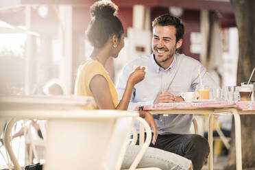 Happy young couple socializing at an outdoor cafe - UUF19245