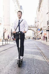 Happy young businessman riding e-scooter in the city, Lisbon, Portugal - UUF19256