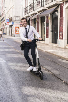 Glücklicher junger Geschäftsmann auf einem E-Scooter in der Stadt, Lissabon, Portugal - UUF19257