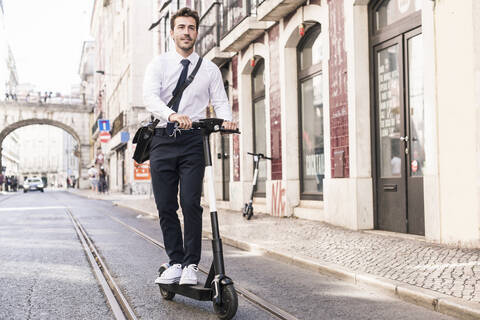 Young businessman riding e-scooter in the city, Lisbon, Portugal stock photo