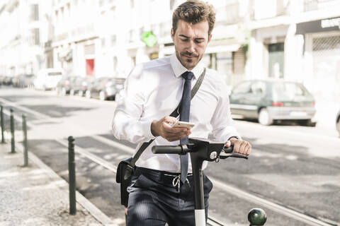 Junger Geschäftsmann mit E-Scooter und Mobiltelefon in der Stadt, Lissabon, Portugal, lizenzfreies Stockfoto