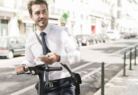 Young businessman with mobile phone and e-scooter in the city, Lisbon, Portugal stock photo