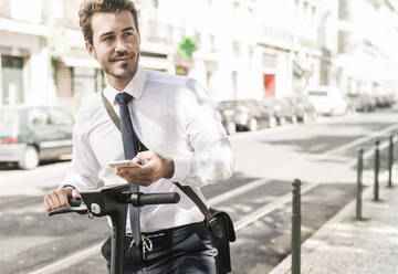 Young businessman with mobile phone and e-scooter in the city, Lisbon, Portugal - UUF19262