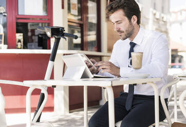 Junger Geschäftsmann mit Tablet und Mobiltelefon in einem Café in der Stadt, Lissabon, Portugal - UUF19264