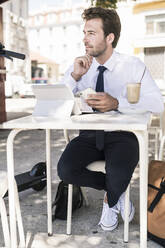 Junger Geschäftsmann mit Tablet und Mobiltelefon in einem Café in der Stadt, Lissabon, Portugal - UUF19265