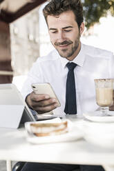 Young businessman using tablet and mobile phone at a cafe in the city, Lisbon, Portugal - UUF19268