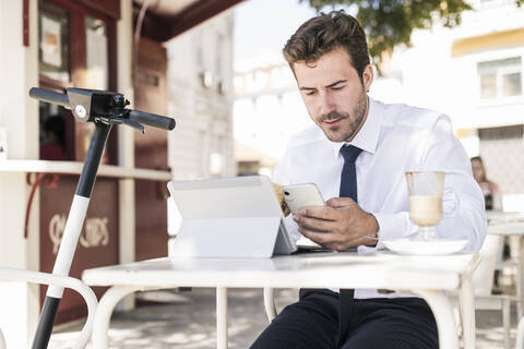 Young businessman using tablet and mobile phone at a cafe in the city, Lisbon, Portugal stock photo