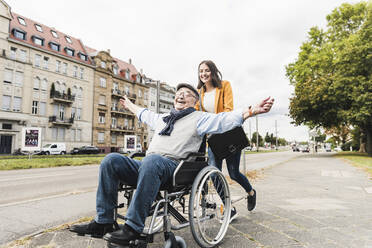 Smiling young woman pushing happy senior man in wheelchair - UUF19274