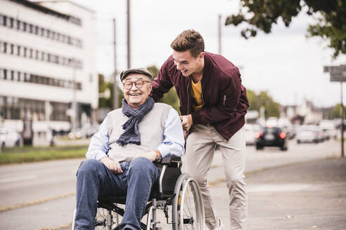 Young man pushing happy senior man in wheelchair - UUF19287