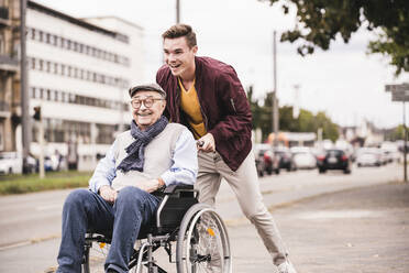 Laughing young man pushing happy senior man in wheelchair - UUF19288