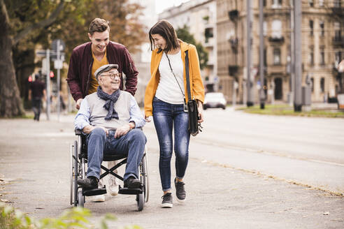 Happy senior man in wheelchair spending time with his grandchildren - UUF19295