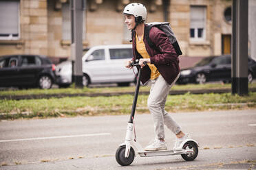 Smiling young man riding scooter in the city - UUF19304