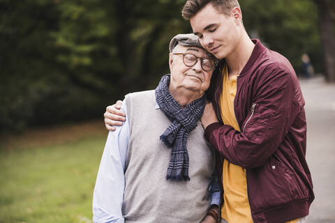 Portrait of senior man head to head with his adult grandson outdoors stock photo