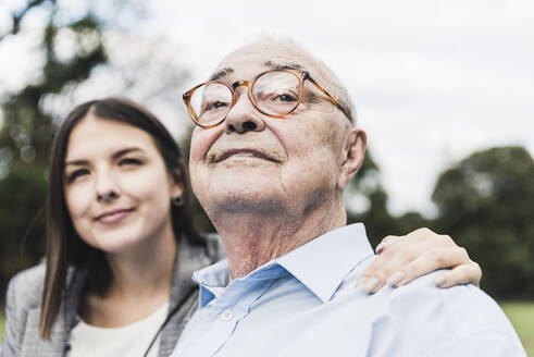 Portrait of self-confident senior man with granddaughter in the background - UUF19322