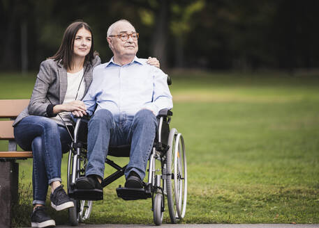 Portrait of senior man in a wheelchair relaxing with granddaughter in a park - UUF19326