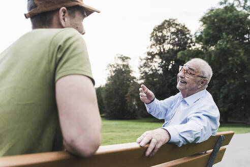 Happy senior man relaxing together with his grandson on a park bench - UUF19327