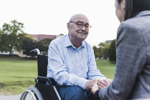 Porträt eines älteren Mannes, der im Rollstuhl sitzt und seine Enkelin an der Hand hält - UUF19330