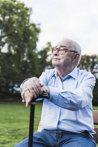 Porträt eines älteren Mannes in einem Park, der sich auf seinen Spazierstock stützt, lizenzfreies Stockfoto