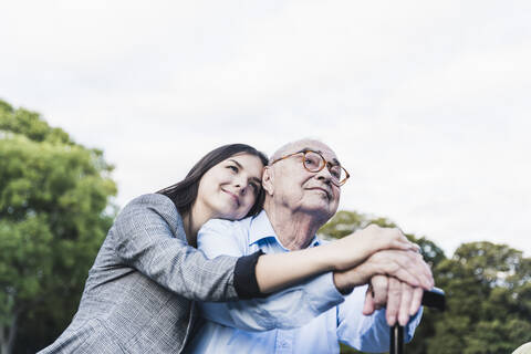 Portrait of young woman hugging her grandfather in a park stock photo