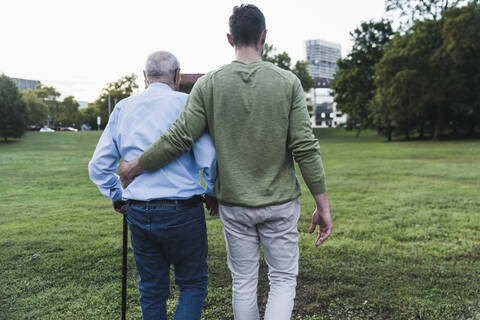 Rückenansicht eines jungen Mannes, der seinem Großvater beim Gehen hilft, lizenzfreies Stockfoto