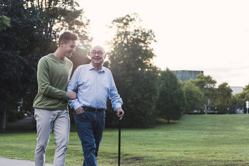 Young man assisting his grandfather walking in a park - UUF19349