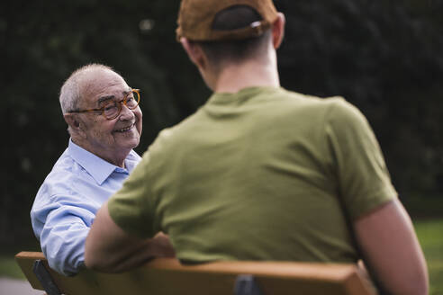 Portrait of smiling senior man relaxing together with his grandson on a park bench - UUF19360