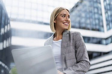 Smiling young businesswoman using laptop in the city - DIGF08637