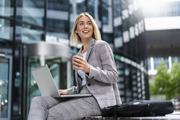 Lächelnde junge Geschäftsfrau mit Laptop in der Stadt - DIGF08638