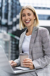 Porträt einer glücklichen jungen Geschäftsfrau mit Laptop in der Stadt - DIGF08640
