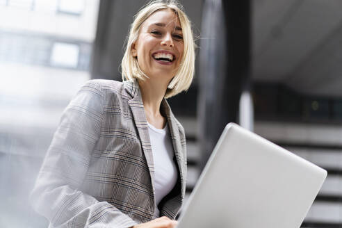 Portrait of happy young businesswoman with laptop in the city - DIGF08641