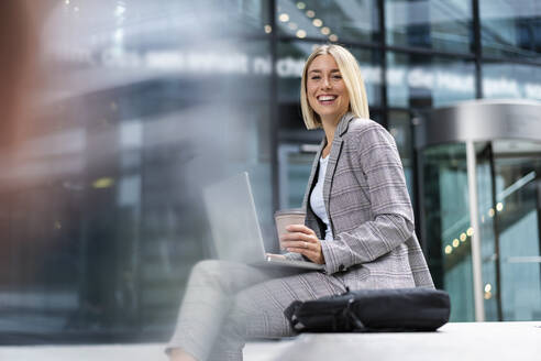 Porträt einer glücklichen jungen Geschäftsfrau mit Laptop in der Stadt - DIGF08642
