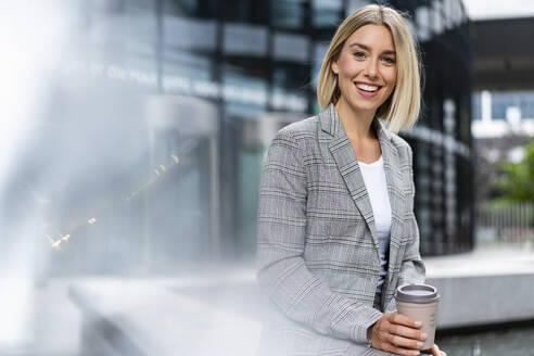 Porträt einer glücklichen jungen Geschäftsfrau mit Kaffee zum Mitnehmen in der Stadt - DIGF08645