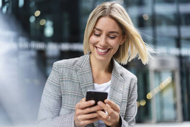 Happy young businesswoman using mobile phone in the city - DIGF08649