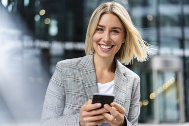 Portrait of happy young businesswoman with mobile phone in the city - DIGF08650