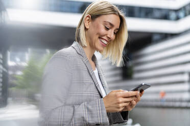 Happy young businesswoman using mobile phone in the city - DIGF08651