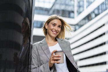 Glückliche junge Geschäftsfrau mit Kaffee zum Mitnehmen in der Stadt - DIGF08655