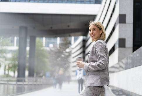 Lächelnde junge Geschäftsfrau mit Kaffee zum Mitnehmen in der Stadt - DIGF08656