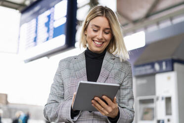 Lächelnde junge Geschäftsfrau mit Tablet am Bahnhof - DIGF08658