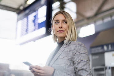 Junge Geschäftsfrau mit Mobiltelefon am Bahnhof - DIGF08659