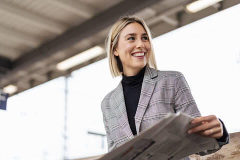 Smiling young businesswoman with newspaper at the train station stock photo