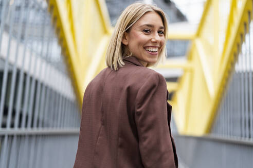 Porträt einer glücklichen jungen Geschäftsfrau auf einer Brücke in der Stadt - DIGF08675